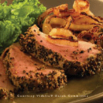 A sumptuous peppercorn-crusted steak is featured prominently, cooked to a medium rare and accompanied by perfectly cooked Vidalia Onions. Fresh leafy greens provide a vibrant contrast to the sizzling, savory meat and golden Vidalia Onions on the plate.